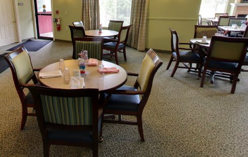 A cozy dining area with several round tables and cushioned chairs arranged on a carpeted floor.