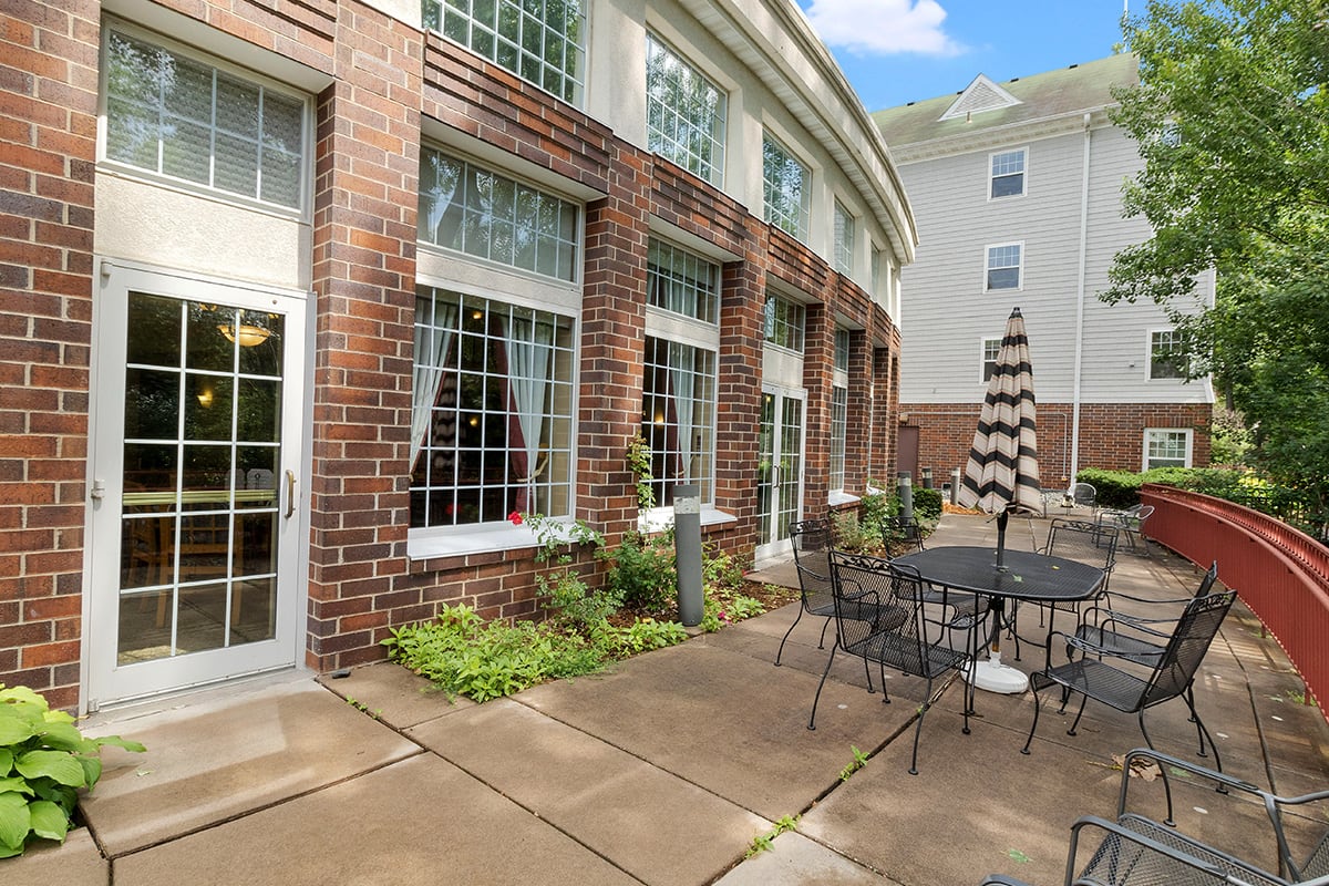 A cozy outdoor patio area with tables, chairs, and an umbrella adjacent to a brick building.
