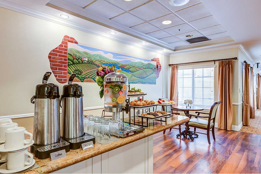 A cozy hotel breakfast buffet featuring coffee dispensers, a juice station, pastries, and a vibrant mural on the wall.