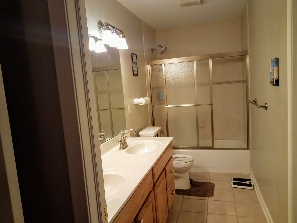 A cozy bathroom with a double sink vanity, glass shower doors, and illuminated mirror.