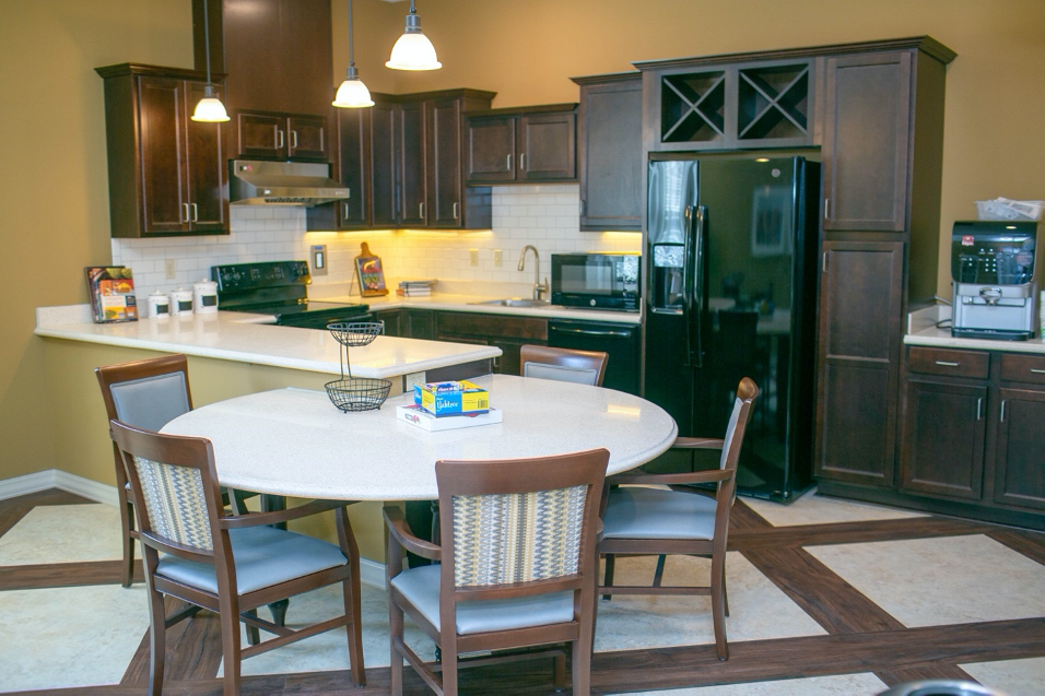 A modern kitchen interior featuring a round dining table, wooden chairs, and sleek dark cabinetry with built-in appliances.