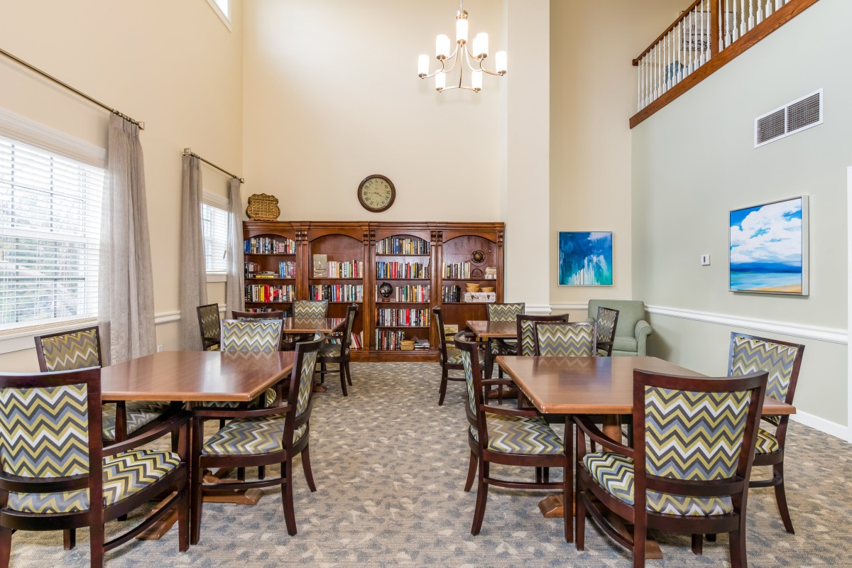 A cozy library reading area featuring bookshelves, tables, and chairs under a chandelier.