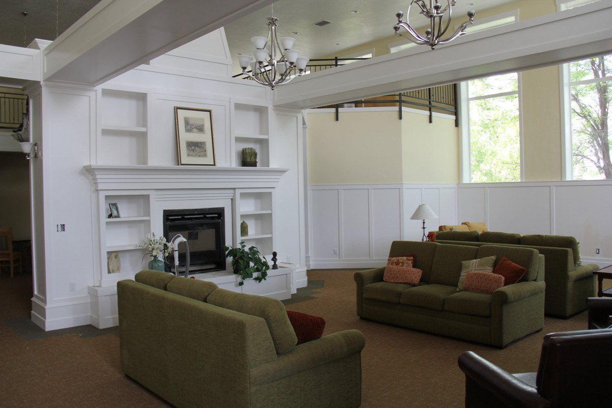 A spacious living room featuring a fireplace, green sofas, chandeliers, and built-in shelves.