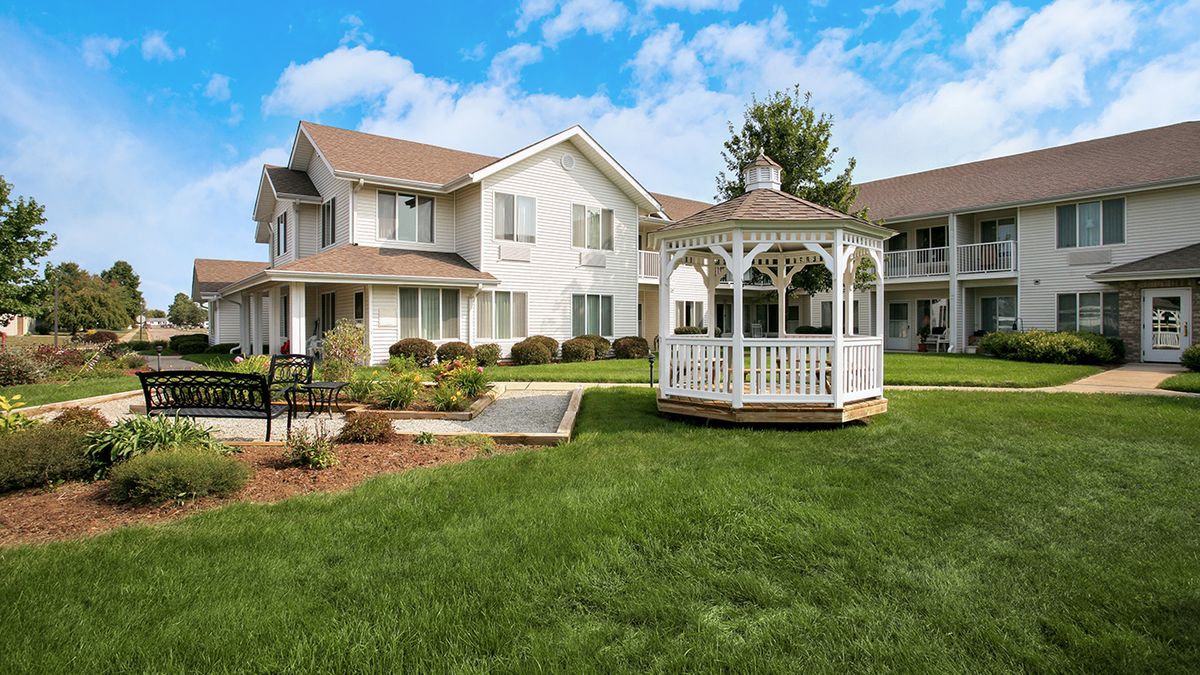 A residential building with a well-maintained lawn and a charming gazebo on a sunny day.