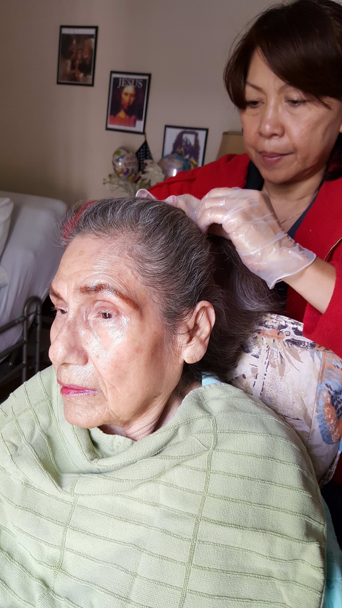An elderly woman is having her hair styled by a caregiver at home.