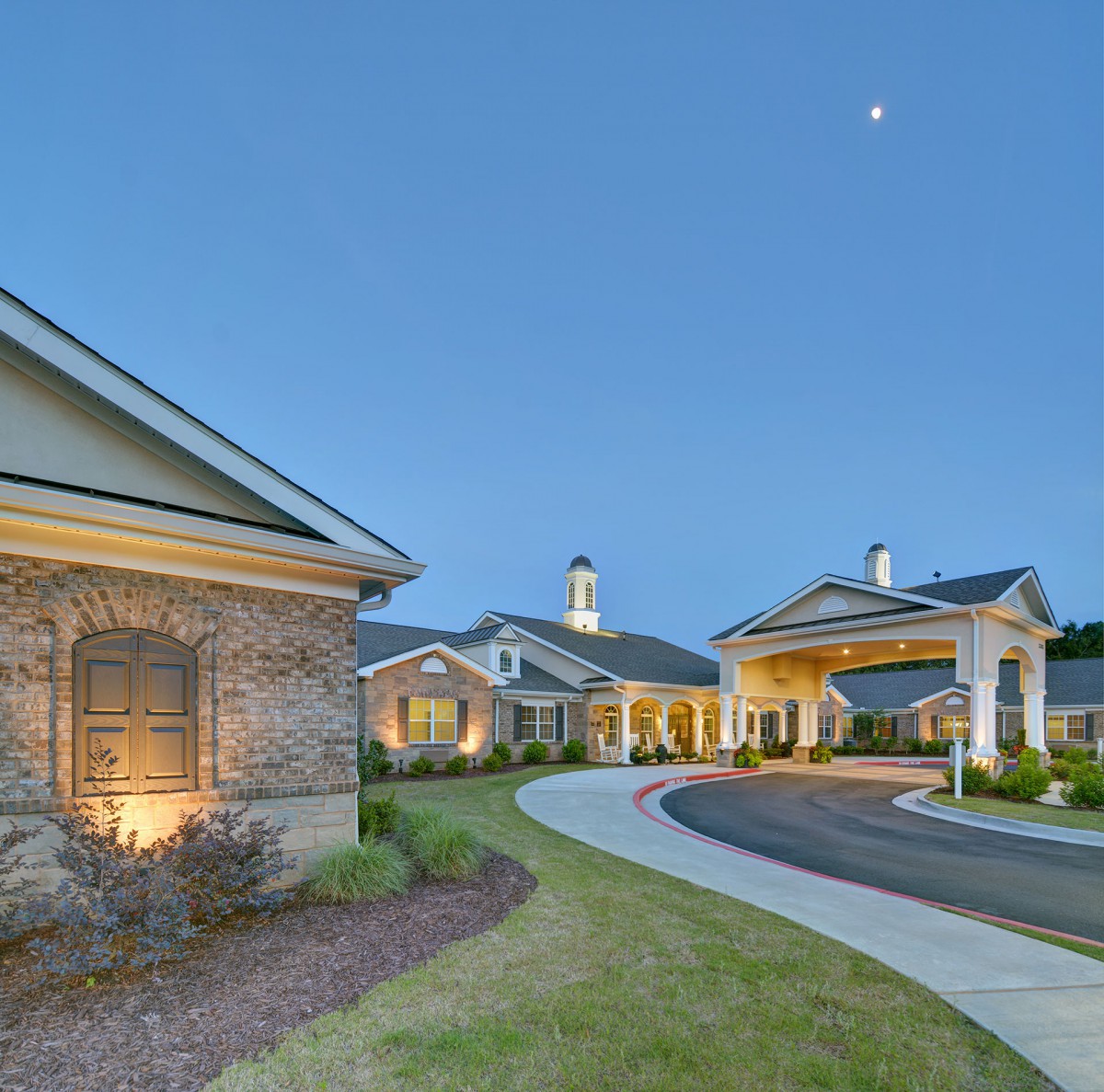 A serene residential building with a well-lit driveway in the evening.