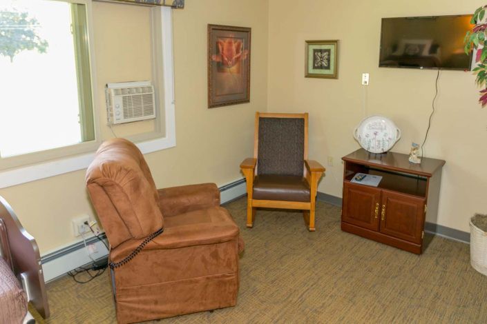 A cozy living room features an armchair, a wooden chair, and wall art.