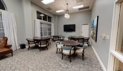 A modern conference room with multiple tables and chairs, a wall-mounted television, and decorative artwork.