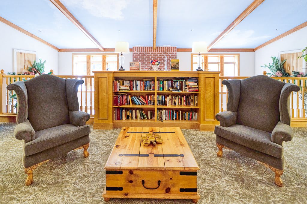 A cozy reading room featuring a wooden bookshelf flanked by armchairs, centered around a rustic coffee table.