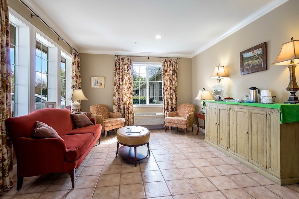 A cozy living room with a red sofa, two armchairs, and a window adorned with patterned curtains.