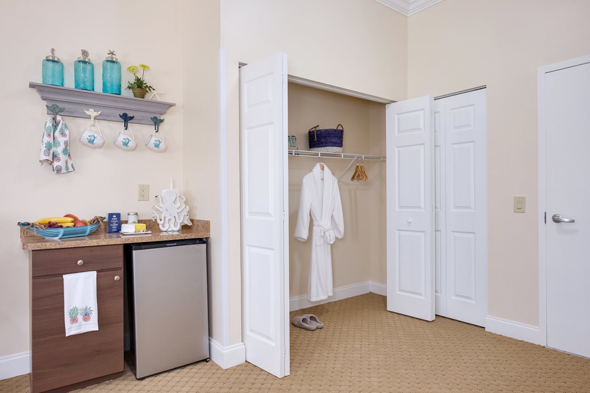 A cozy room with an open closet featuring a hanging robe and a mini fridge nearby.