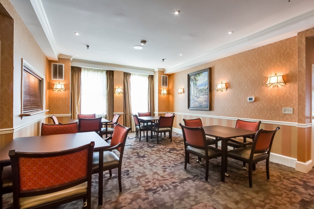 A dining room with several tables and chairs, featuring warm lighting and artwork on the walls.