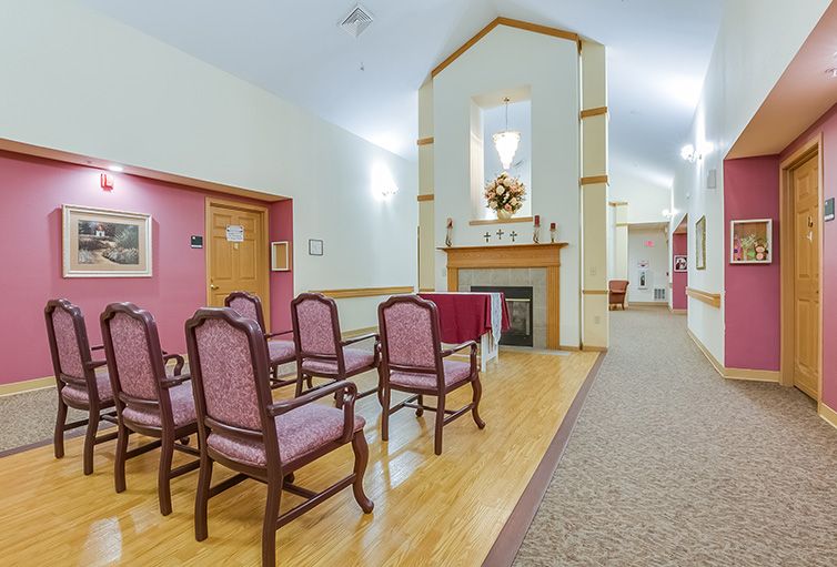 A small chapel room with neatly arranged chairs facing a decorative fireplace.