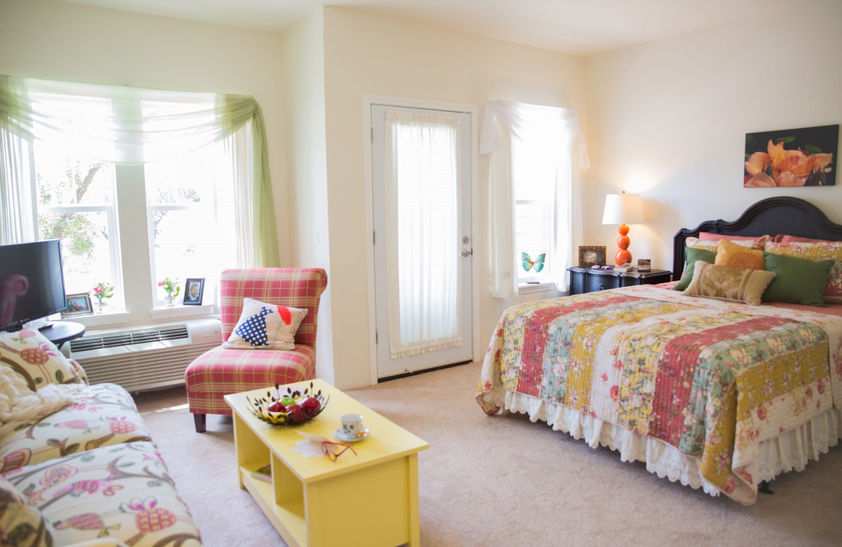 A cozy bedroom with colorful decor, featuring a bed and a chair bathed in natural light.