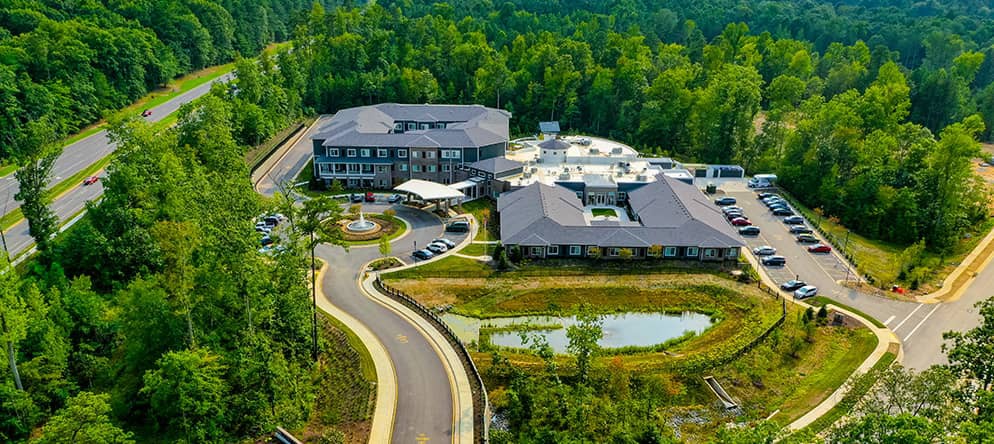 Aerial view of a building complex surrounded by nature and a winding road.