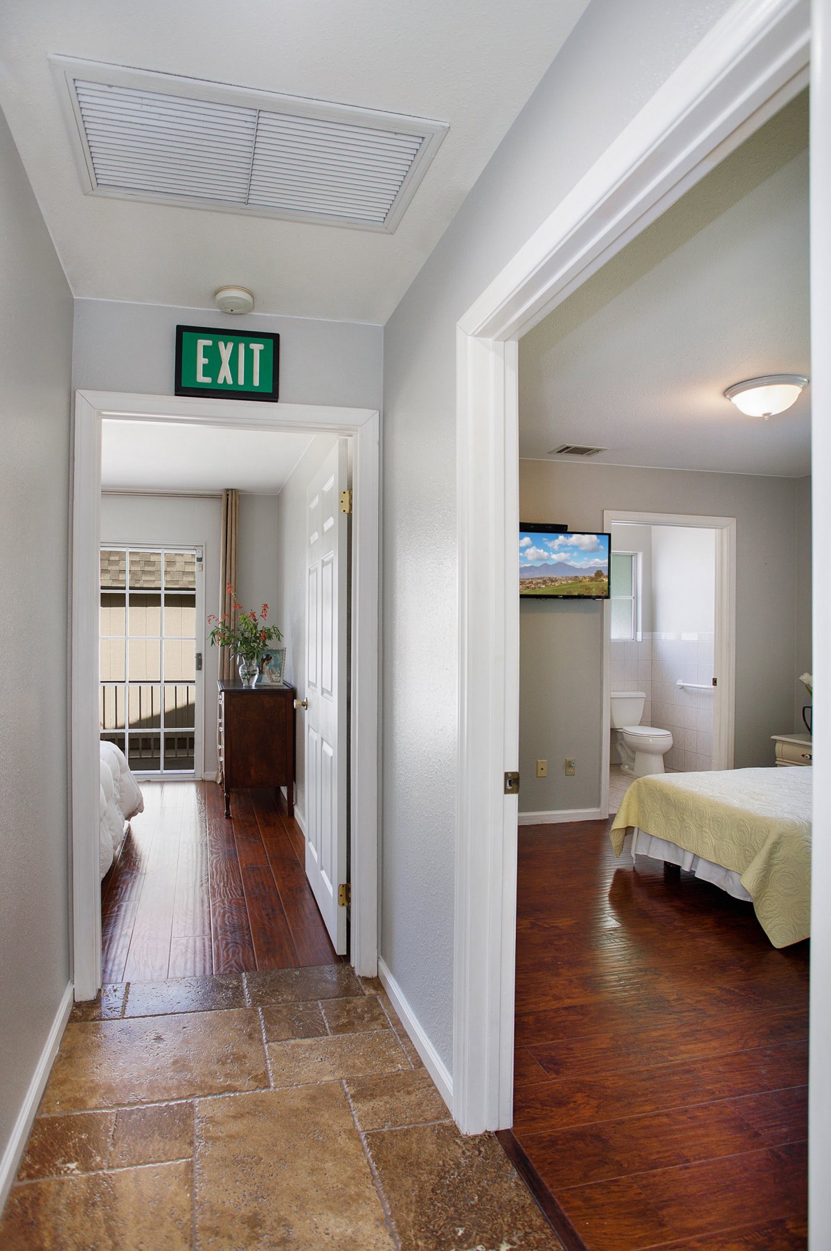A hallway with wooden flooring leading to bedrooms, featuring an exit sign and ample natural light.