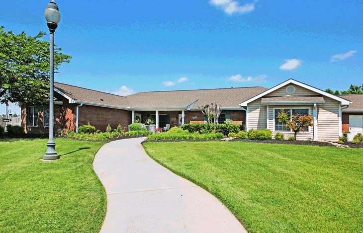 A suburban house with a well-manicured lawn and a winding pathway under a clear blue sky.