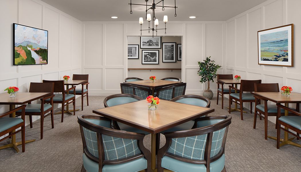 A cozy dining room with neatly arranged tables and chairs, featuring a decorative chandelier and wall art.