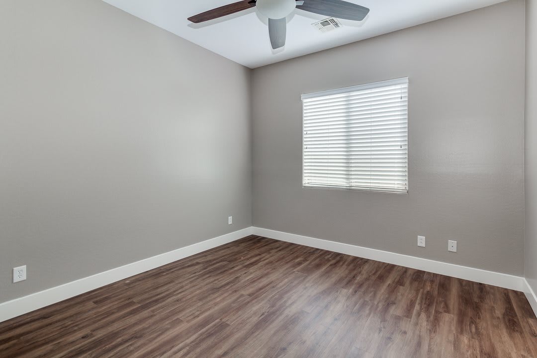 An empty room featuring wood flooring, a ceiling fan, and window blinds.
