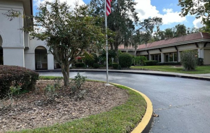 A driveway leading to a building with an American flag and surrounding greenery.