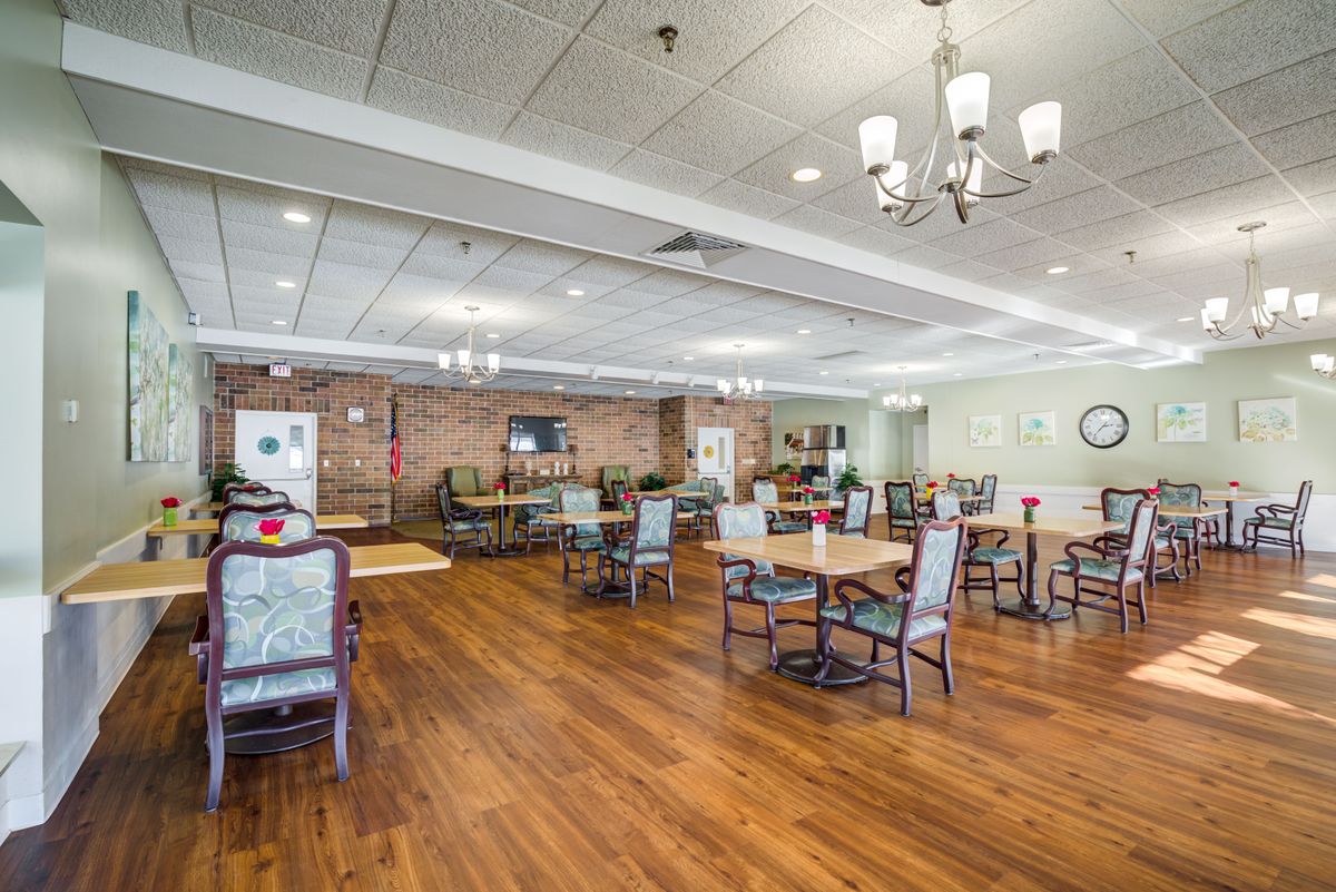 A spacious dining area with wooden flooring, furnished with neatly arranged tables and chairs.