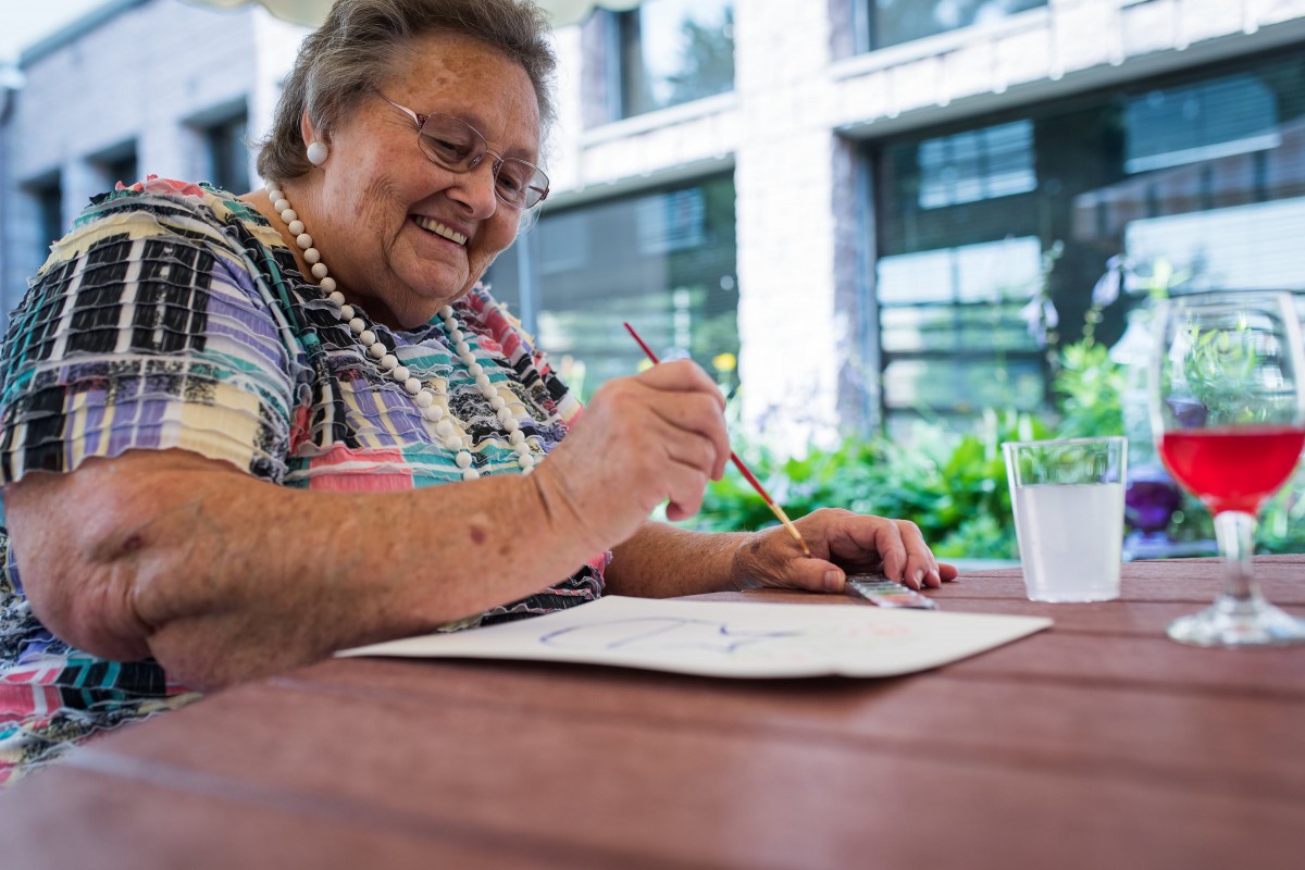 An elderly woman enjoying a painting session outdoors, smiling as she creates art.