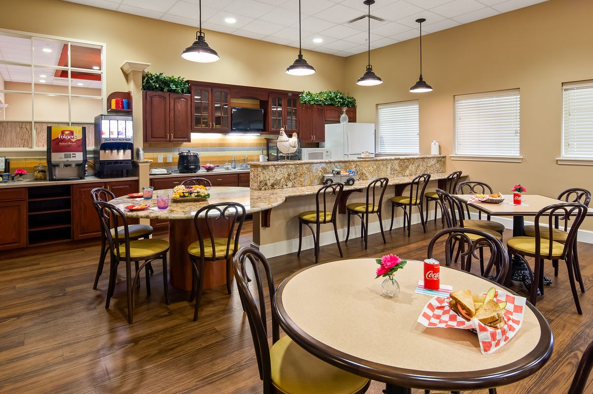 A cozy cafe dining area with round tables, chairs, pendant lights, and a beverage station.