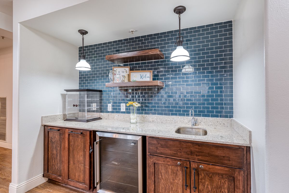 A modern kitchen setup featuring a blue tiled backsplash, wooden cabinets, and open shelves with pendant lighting.