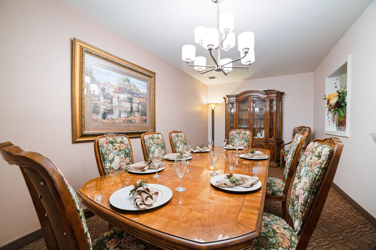 A neatly set dining room table with a chandelier above and a decorative painting on the wall.