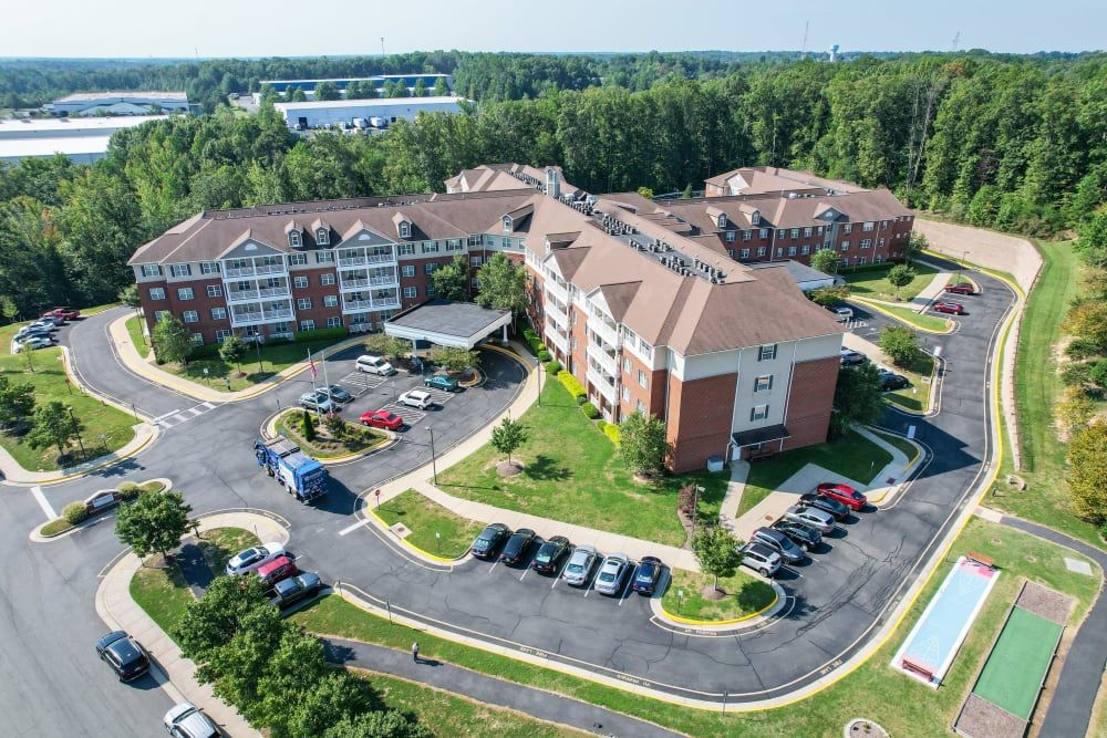 Aerial view of a large residential building surrounded by greenery and parking spaces.