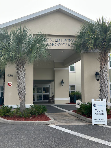 Entrance of a memory care facility with palm trees lining the pathway.