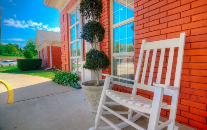 A peaceful porch with a white rocking chair and potted plants in front of a red brick wall.