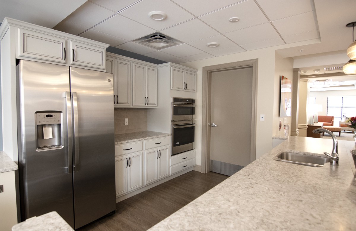 A modern kitchen interior featuring white cabinets, a stainless steel refrigerator, and built-in ovens.