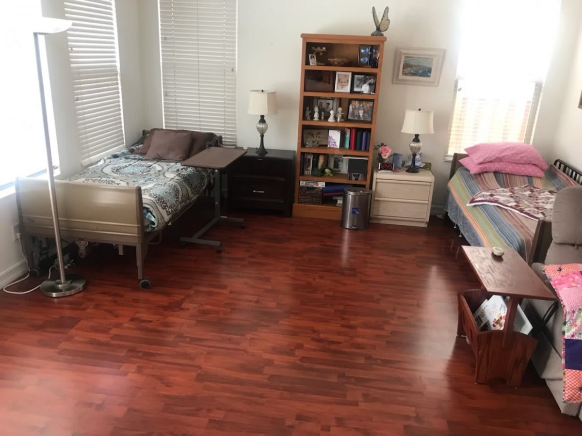 A tidy bedroom with two beds, hardwood flooring, and a bookshelf.