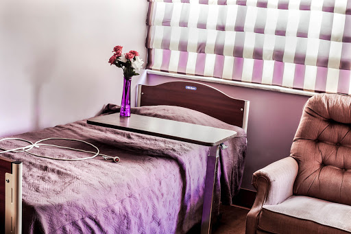 A cozy hospital room featuring a neatly made bed, a bedside table, and fresh flowers in a purple vase.