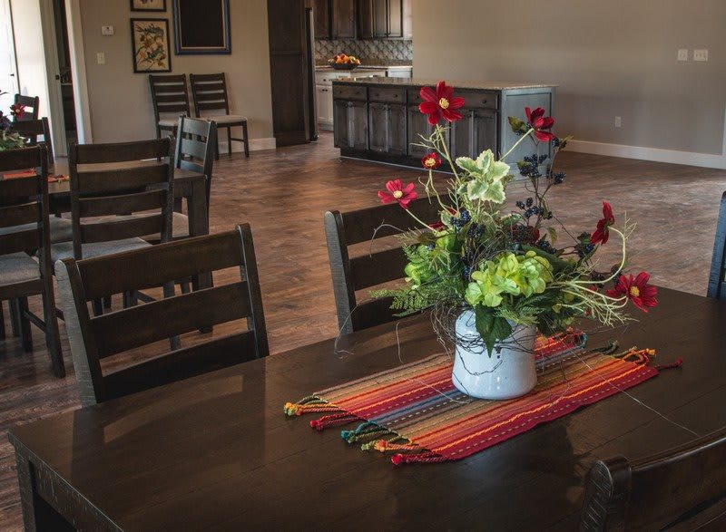A cozy dining area with a flower arrangement centerpiece on the table, leading into an open kitchen space.