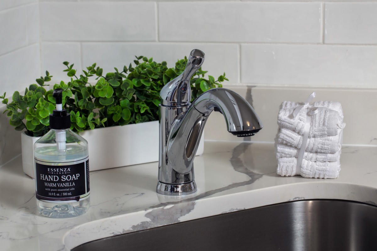 A modern kitchen sink setup with a chrome faucet, plants, and accessories.
