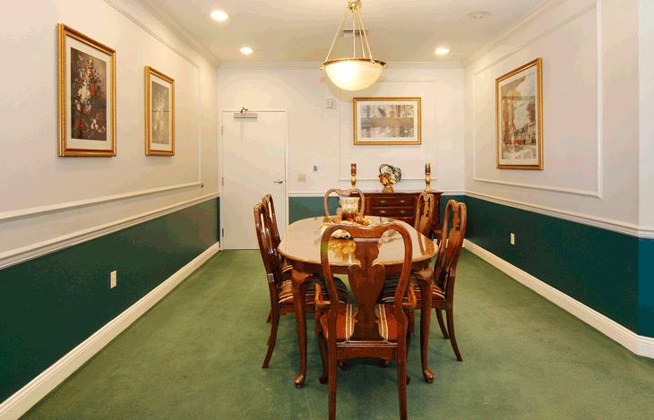 A traditional dining room with a wooden table and chairs, illuminated by a chandelier and adorned with wall art.