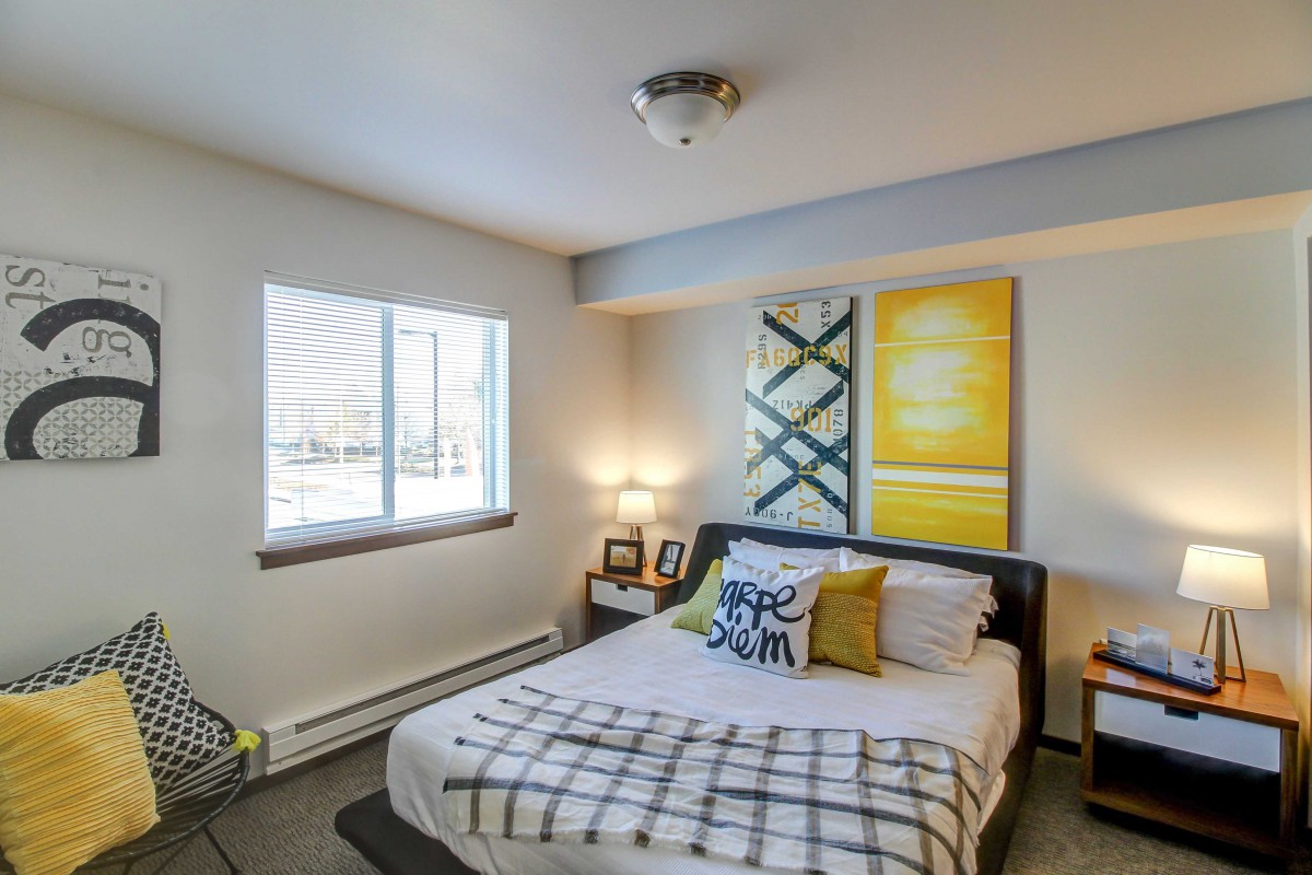 A cozy bedroom with a neatly made bed, modern artwork, and ample natural light.