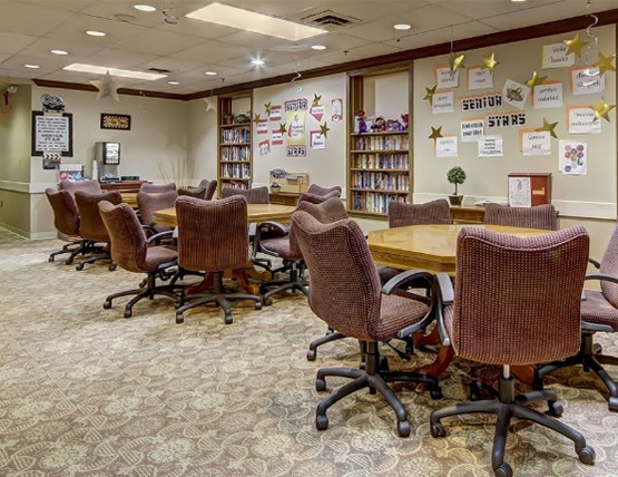 A spacious conference room with multiple tables and chairs, surrounded by bookshelves and decorated walls.