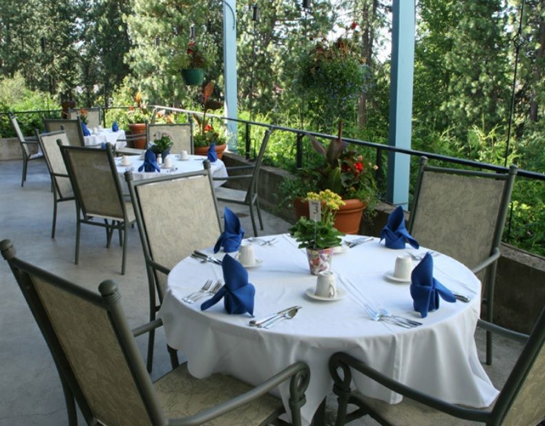 A beautifully set table on an outdoor restaurant patio surrounded by lush greenery and flowers.