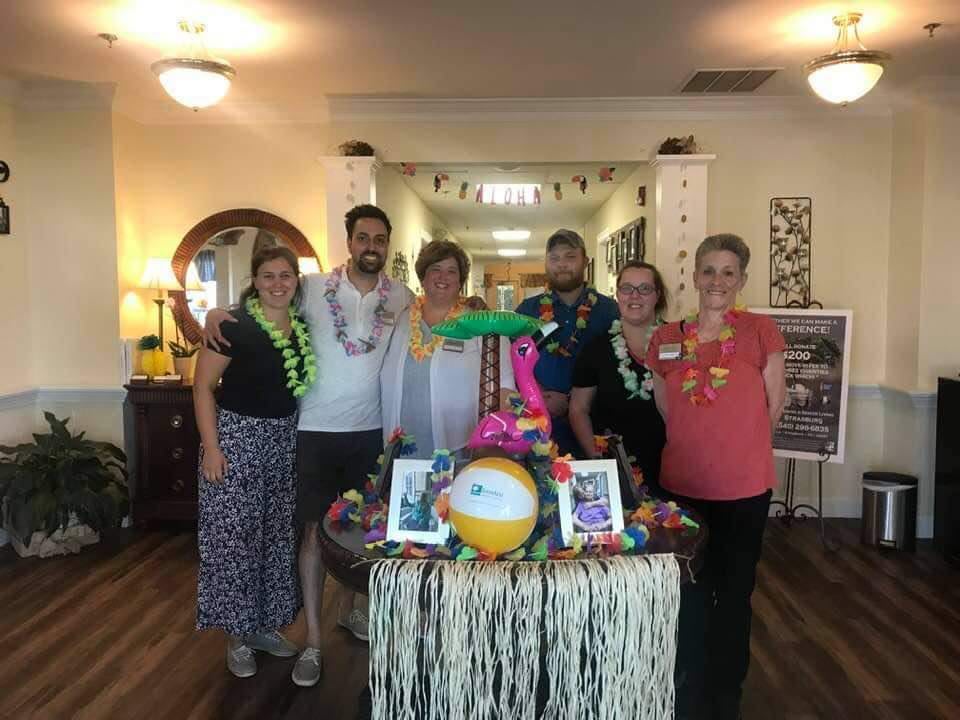 A group of people standing around a decorated table with a tropical theme in an indoor setting.