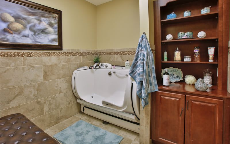 A bathroom with an accessible bathtub, surrounded by tiled walls and a wooden shelf stocked with toiletries.