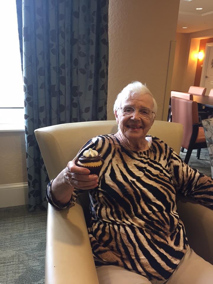 An elderly woman smiling while sitting in an armchair, wearing a zebra print dress.