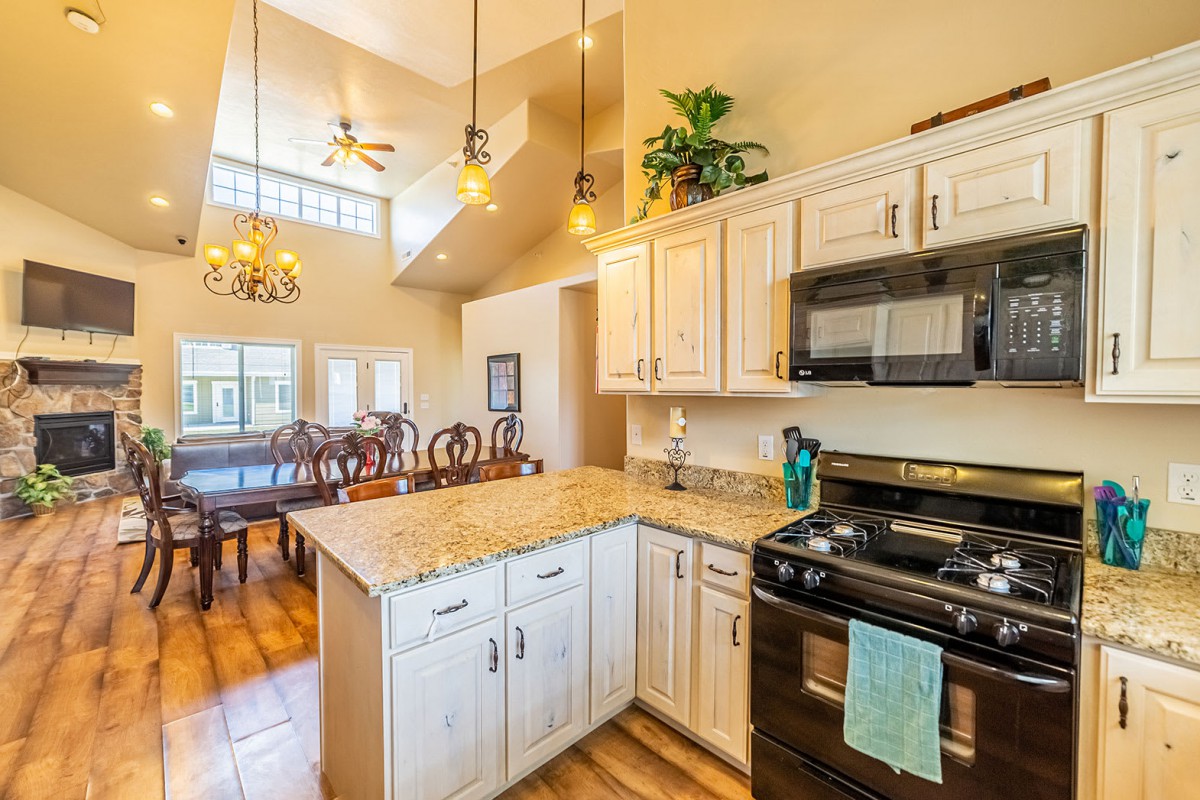 A modern kitchen with an open layout leading to a dining area, featuring granite countertops and pendant lighting.