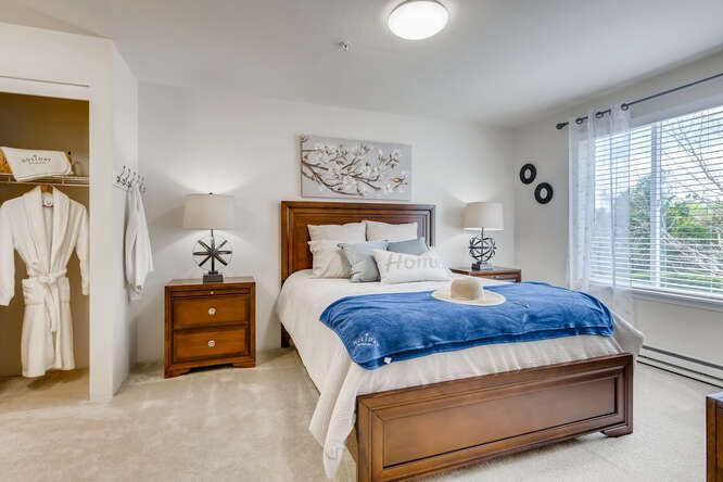 A modern and cozy bedroom featuring a neatly made bed with a blue blanket, flanked by wooden nightstands and stylish lamps. The room is decorated with wall art above the headboard.