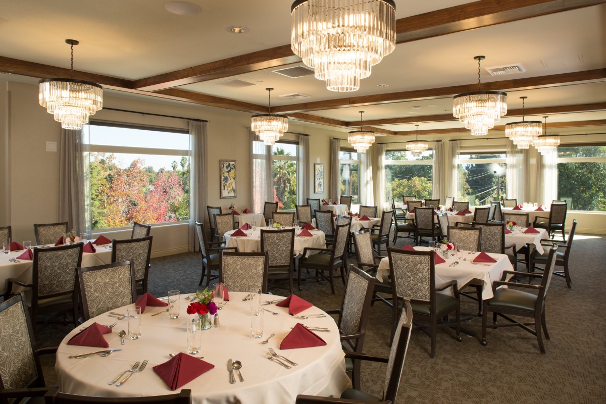 An elegant banquet hall with round tables set for dining, featuring chandeliers and large windows overlooking a scenic view.