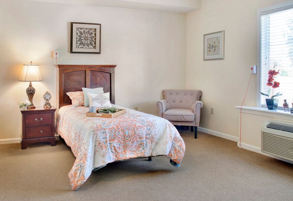 A cozy bedroom with a single bed and an armchair, featuring simple decor and soft lighting.