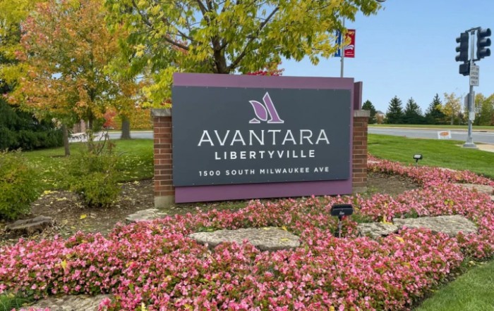 Entrance sign for Avantara Libertyville surrounded by colorful flowers and trees.