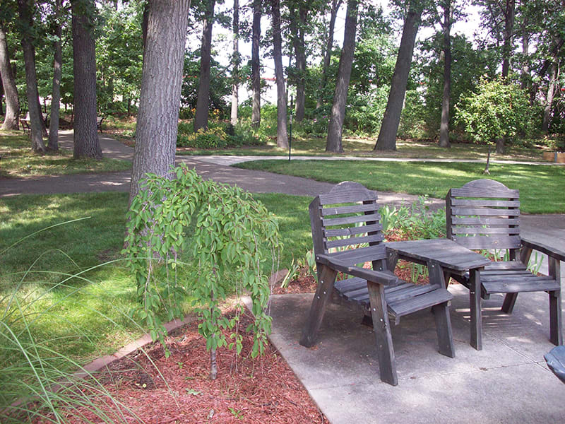 A peaceful garden setting with wooden chairs and a table surrounded by trees.